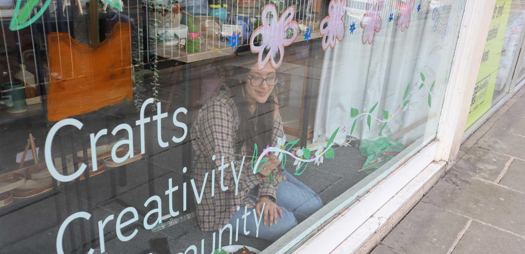 aaliyah smiling and painting leaves and flowers onto our shop window with acrylic paint 